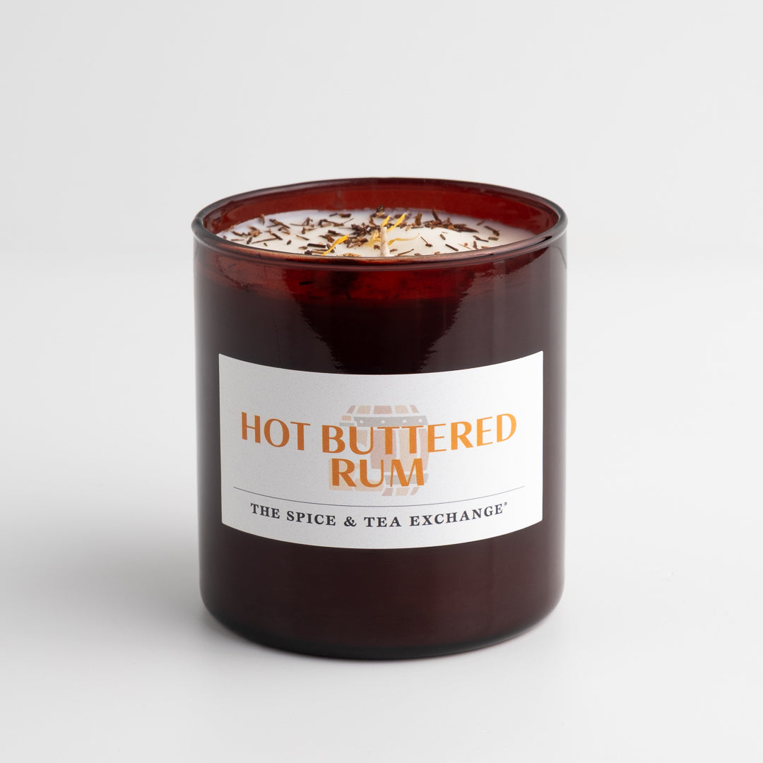 Hot buttered rum candle in a glass container with a label on a white background